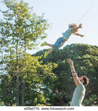 Stock Image - Father throwing son in air, outdoors. Fotosearch