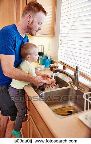 Stock Image - Father washing son's hands in kitchen sink. Fotosearch