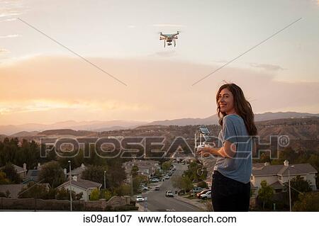 Female commercial operator flying drone above housing development, looking over shoulder at camera, Santa Clarita, California, USA View Large Photo Image Stock Photo - Female commercial operator flying drone above housing development, looking over shoulder at camera, Santa Clarita, California, USA. Fotosearch