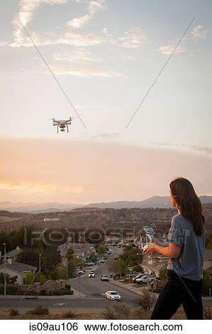 Stock Photograph - Female commercial operator flying drone above housing development, Santa Clarita, California, USA. Fotosearch