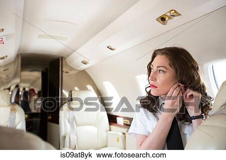 Female flight attendant putting on earring in cabin of private jet View Large Photo Image Stock Image - Female flight attendant putting on earring in cabin of private jet. Fotosearch