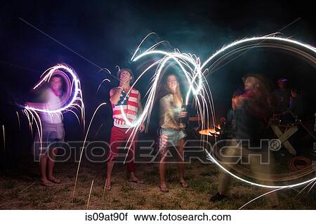 Stock Image - Four adult friends celebrating with sparklers in darkness on Independence Day, USA. Fotosearch