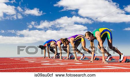 Stock Image - Four female athletes on starting blocks, about to start race. Fotosearch