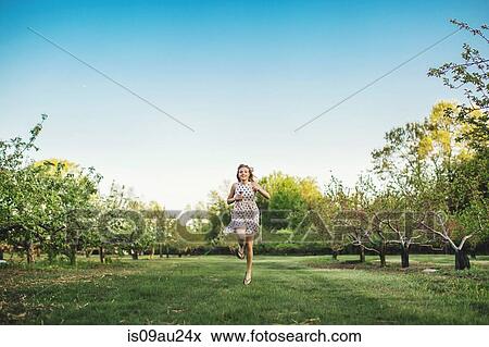 Full length front view of young woman wearing sleeveless dress running through orchard, looking at camera smiling View Large Photo Image Stock Photo - Full length front view of young woman wearing sleeveless dress running through orchard, looking at camera smiling. Fotosearch