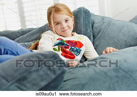 Stock Image - Girl lying on pile of cushions in living room. Fotosearch