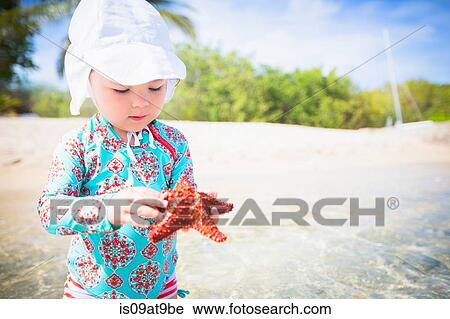 Girl on beach wearing swimear and sunhat holding starfish looking down, St. Croix, US Virgin Islands View Large Photo Image Stock Image - Girl on beach wearing swimear and sunhat holding starfish looking down, St. Croix, US Virgin Islands. Fotosearch