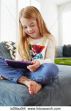 Girl using digital tablet on sofa in living room View Large Photo Image Picture - Girl using digital tablet on sofa in living room. Fotosearch