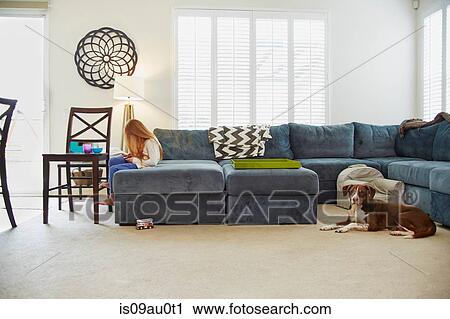 Girl using digital tablet on sofa in living room, dog behind her View Large Photo Image Stock Image - Girl using digital tablet on sofa in living room, dog behind her. Fotosearch