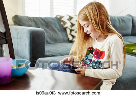 Stock Image - Girl using digital tablet on sofa in living room. Fotosearch