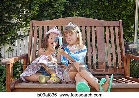 Stock Photograph - Girls enjoying ice lolly on garden bench. Fotosearch