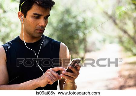 Jogger selecting music on smartphone in park View Large Photo Image Stock Photo - Jogger selecting music on smartphone in park. Fotosearch