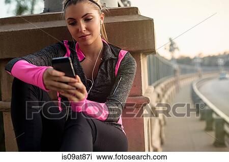 Stock Image - Jogger using cellular phone on bridge, Arroyo Seco Park, Pasadena, California, USA. Fotosearch