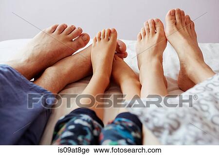 Stock Image - Legs and bare feet of parents and son lying in bed. Fotosearch