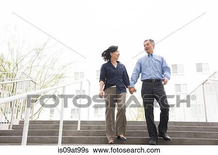 Stock Photograph - Low angle full length front view of mature couple holding hands descending stairs. Fotosearch
