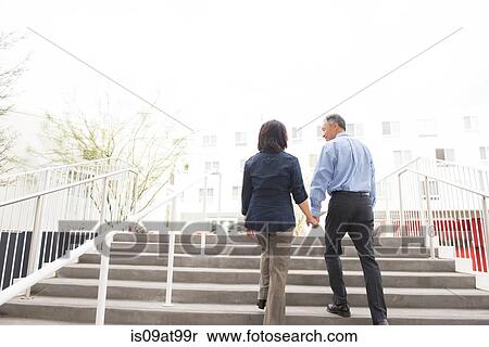 Low angle full length rear view of mature couple holding hands ascending stairs View Large Photo Image Stock Photography - Low angle full length rear view of mature couple holding hands ascending stairs. Fotosearch