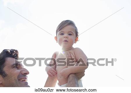 Low angle view of father holding up son, looking at camera View Large Photo Image Stock Photography - Low angle view of father holding up son, looking at camera. Fotosearch
