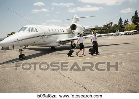 Stock Image - Male and female private jet pilots leaving plane at airport. Fotosearch
