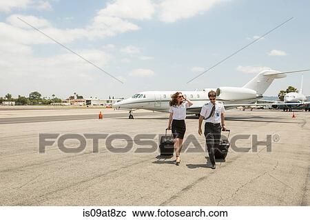 Stock Image - Male and female private jet pilots arriving at airport. Fotosearch
