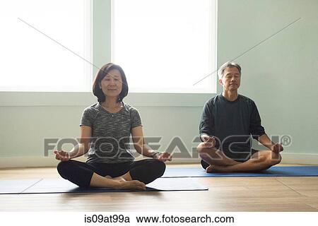 Stock Image - Mature couple sitting cross legged on yoga mat meditating eyes closed. Fotosearch