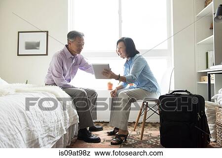 Mature couple sitting in hotel room with suitcase using digital tablet View Large Photo Image Stock Photo - Mature couple sitting in hotel room with suitcase using digital tablet. Fotosearch