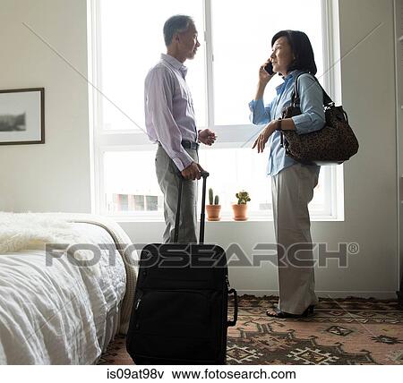 Mature couple standing in hotel room with suitcase using cellular phone View Large Photo Image Stock Photo - Mature couple standing in hotel room with suitcase using cellular phone. Fotosearch