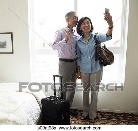 Mature couple standing in hotel room using smartphone to take selfie smiling View Large Photo Image Stock Photo - Mature couple standing in hotel room using smartphone to take selfie smiling. Fotosearch