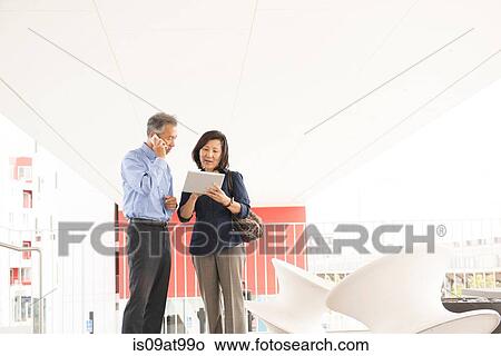 Mature couple standing using digital tablet and smartphone, looking down View Large Photo Image Picture - Mature couple standing using digital tablet and smartphone, looking down. Fotosearch
