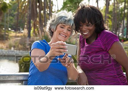 Mature female friends in park, looking at smartphone, laughing View Large Photo Image Stock Photo - Mature female friends in park, looking at smartphone, laughing. Fotosearch