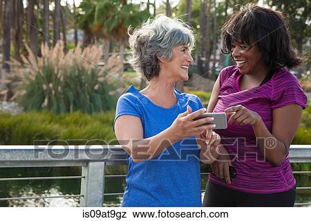 Mature female friends in park, looking at smartphone, laughing View Large Photo Image Stock Photo - Mature female friends in park, looking at smartphone, laughing. Fotosearch