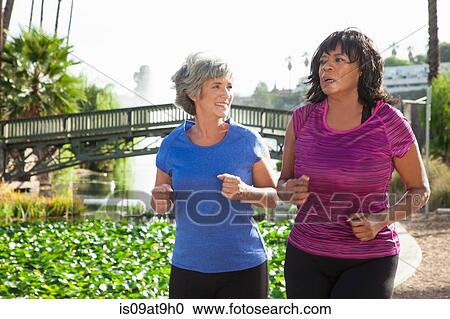 Stock Image - Mature female friends jogging in park. Fotosearch