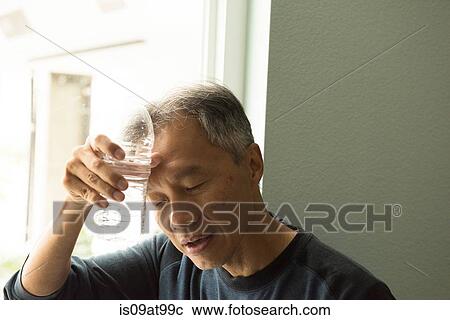 Stock Image - Mature man holding bottle of water to forehead eyes closed. Fotosearch