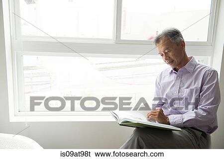 Mature man sitting in front of window reading book View Large Photo Image Stock Photograph - Mature man sitting in front of window reading book. Fotosearch
