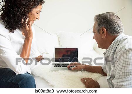 Mature woman and husband looking at laptop on bed View Large Photo Image Stock Image - Mature woman and husband looking at laptop on bed. Fotosearch