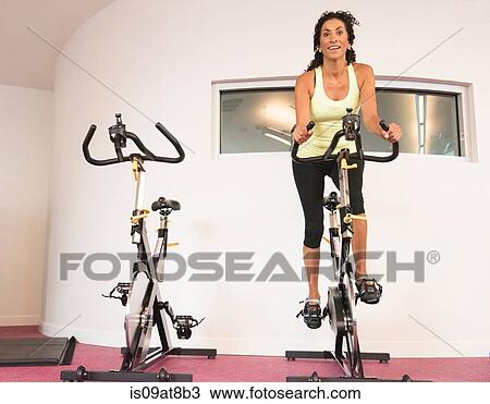 Stock Image - Mature woman at gym on exercise bicycle. Fotosearch