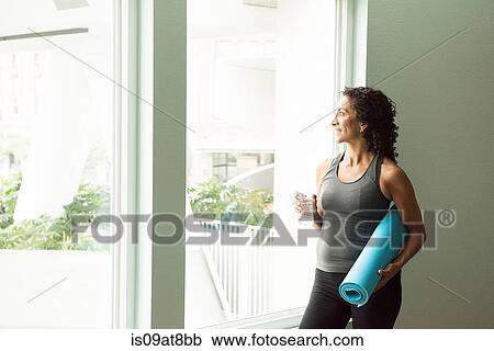 Stock Image - Mature woman drinking water after yoga. Fotosearch