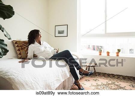 Stock Photo - Mature woman relaxing on bed drinking coffee. Fotosearch