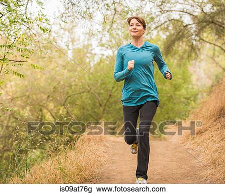 Stock Image - Mature woman running through forest. Fotosearch