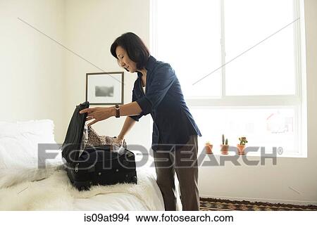 Picture - Mature woman standing in hotel room packing suitcase. Fotosearch