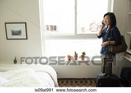 Mature woman standing in hotel room with suitcase using smartphone View Large Photo Image Stock Image - Mature woman standing in hotel room with suitcase using smartphone. Fotosearch