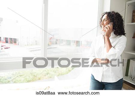 Mature woman talking on smartphone at apartment window View Large Photo Image Stock Image - Mature woman talking on smartphone at apartment window. Fotosearch