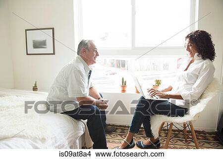 Picture - Mature woman using laptop whilst and husband on bed. Fotosearch