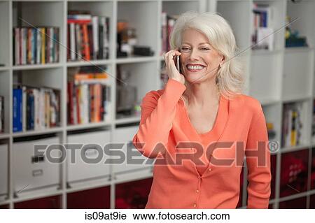 Stock Image - Mature woman using mobile phone, indoors. Fotosearch