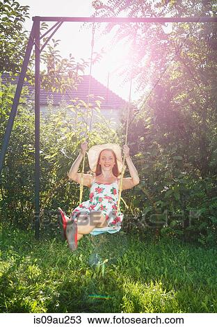 Stock Image - Mid adult woman swinging on garden swing. Fotosearch