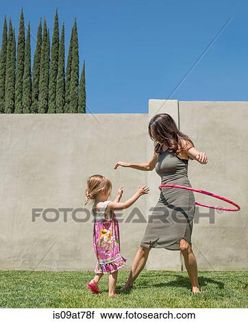 Stock Image - Mother and daughter playing with plastic hoop in garden. Fotosearch