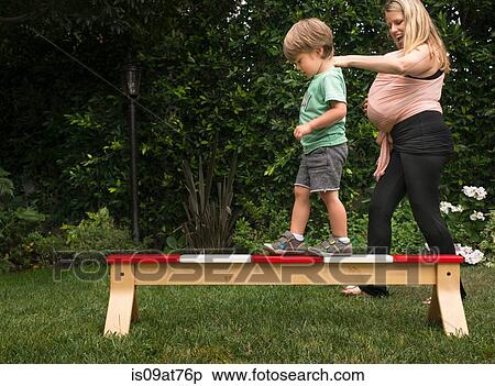 Stock Photography - Mother helping son walk across balance bar in garden. Fotosearch