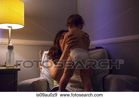 Stock Photo - Mother in armchair holding up baby boy wearing nappy. Fotosearch