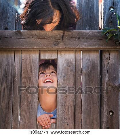 Mother looking over at son, through hole in fence View Large Photo Image Picture - Mother looking over at son, through hole in fence. Fotosearch