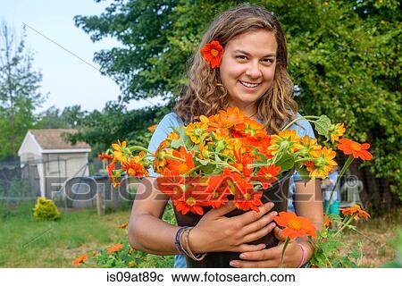 Stock Image - Portrait of female farm worker holding a bucket of fresh cut flowers. Fotosearch
