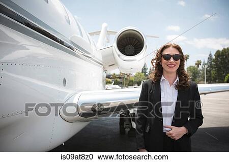 Stock Image - Portrait of mid adult female businesswoman and private jet at airport. Fotosearch