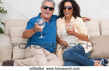 Stock Photograph - Portrait of senior man and wife sitting on patio sofa. Fotosearch